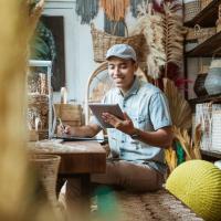 Male small business owner behind shop counter using mobile device.