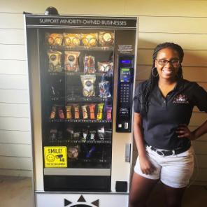 Aerika Mikes i AM brown Originations founder next to vending machine.