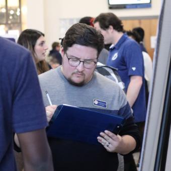 A student holds a clipboard, intently writing something down.