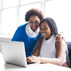 A mother and daughter sitting in front of a laptop and discussing what is on the screen.